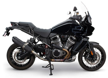 A black motorcycle with a tall windshield and dual exhausts is parked on a stand. The bike features a robust frame and spoked wheels.