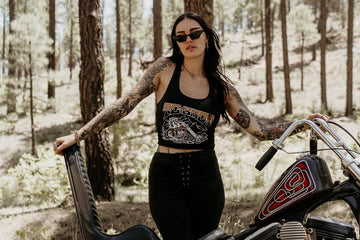 A woman with tattoos posing in front of a brick wall.