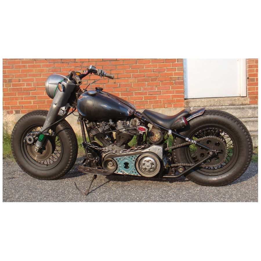 A motorcycle parked in front of a brick building, with a Monster Craftsman Bolt On Chain Tensioner - Skate Wheel (Powell Peralta) drive chain.
