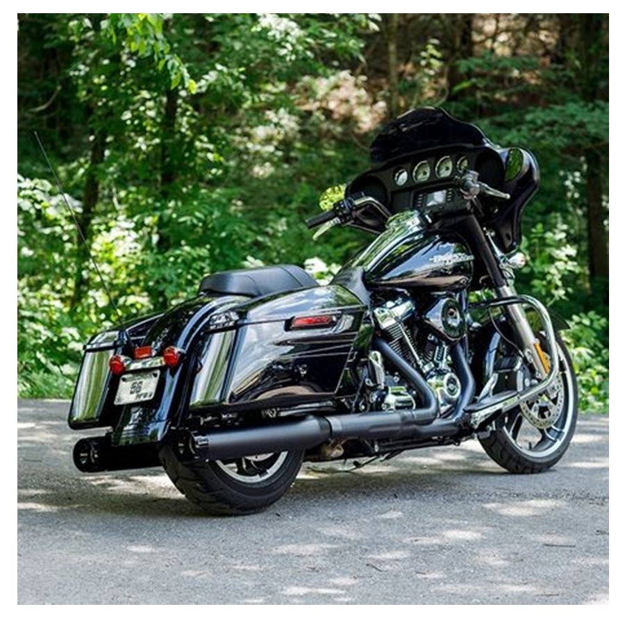 A black motorcycle is parked on a road in the woods, showcasing its S&S Cycle 50 State Legal - Mk45 TOURING MUFFLER for M8 TOURING MODELS - Black with Black Thruster End Cap.