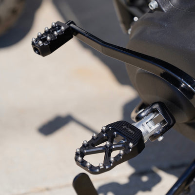 A close up of the TC Bros. Pro Series Black MX Rider Foot Pegs for 2018-newer Harley Softail & Pan America, featuring high traction and stability.