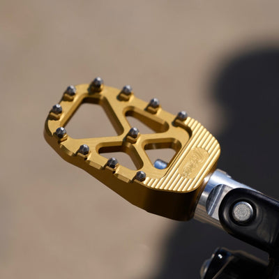 A close up of TC Bros. Pro Series Gold MX Rider Foot Pegs for a 2018-newer Harley Softail & Pan America rider, providing high traction and stability.