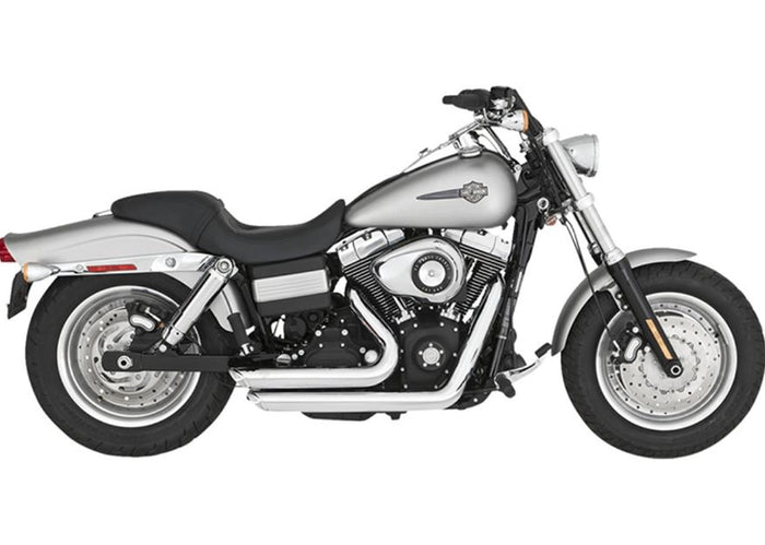 A silver and black cruiser-style motorcycle with chunky tires, a chrome Vance & Hines Short Shots Exhaust System for 06-09 Fat Bob, Dyna, Low, Wide & Super Glide, and a single seat, viewed from the rear left side.