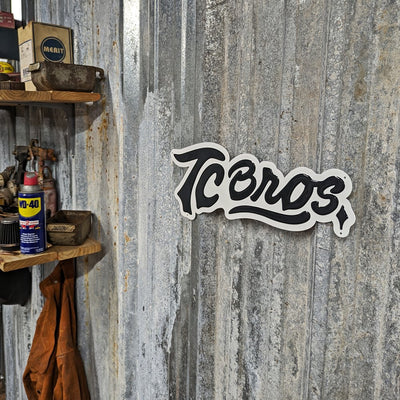 A TC Bros. Metal Shop Sign - Stamped Aluminum with the word "icons" in a cursive font, affixed to a textured gray stamped aluminum surface.