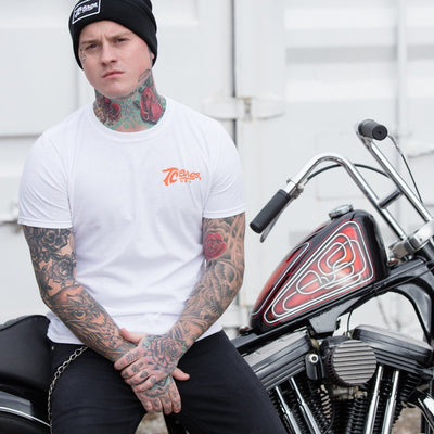 A White man with tattoos sitting on a TC Bros. Classic T-Shirt motorcycle.
