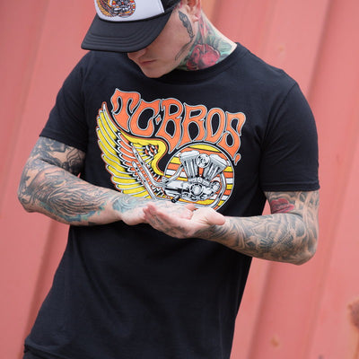 A man wearing a black TC Bros. Wing T-Shirt with tattoos.