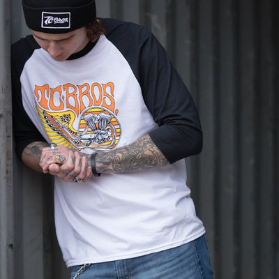 A man with tattoos is leaning against a wall, wearing the TC Bros. Wing Raglan - White/Black shirt by TC Bros.
