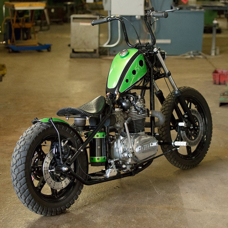 A green and black TC Bros. motorcycle parked in a garage with removable caps.