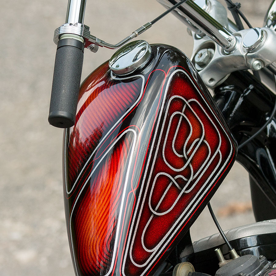 A close up of a motorcycle with a red and black paint job featuring the Moto Iron® Cam Lock Gas Cap, a chrome plated steel vented gas cap.