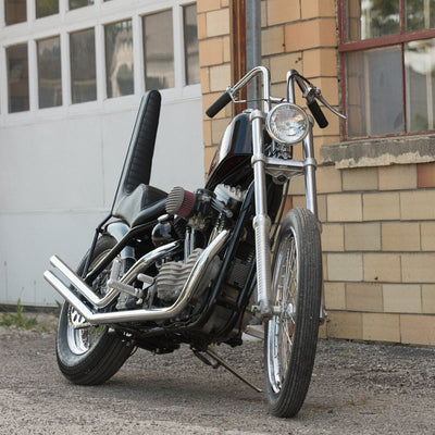 A motorcycle with a Moto Iron® Harley Sportster Upsweep Exhaust Pipes for '86-'03 parked in front of a brick building.