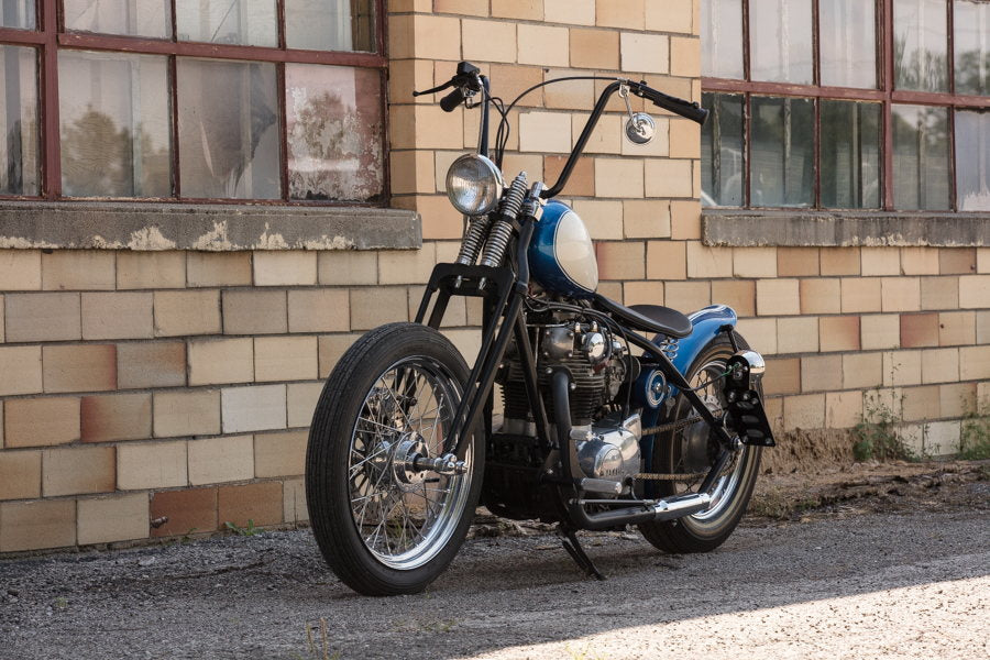 A blue and black motorcycle with TC Bros. 7/8" Ape Hanger Handlebars - 12" Black Powdercoated parked in front of a brick building.