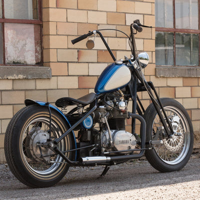 A blue and black TC Bros. Chopper motorcycle parked in front of a building with removable caps.
