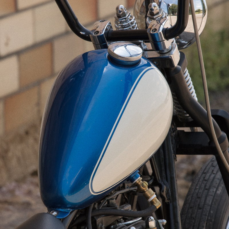 A Moto Iron® 2.2 Gal. Axed Tank chopper motorcycle parked in front of a brick wall.