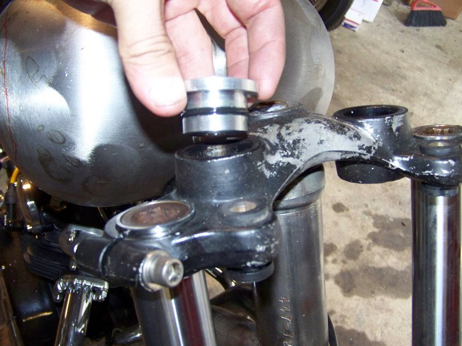 A person is adjusting the handlebars on a Hughs HandBuilt Yamaha XS650 motorcycle, using Hughs HandBuilt solid riser bushings.