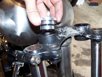 A person is adjusting the handlebars on a Hughs HandBuilt Yamaha XS650 motorcycle, using Hughs HandBuilt solid riser bushings.