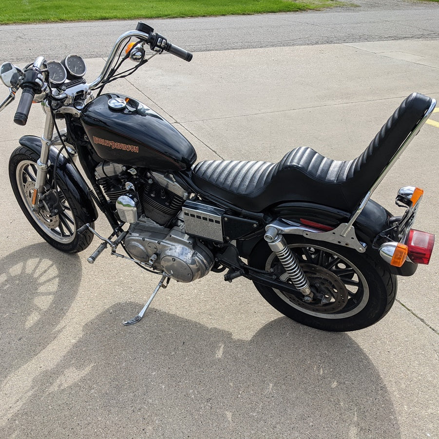 A TC Bros. Sportster King & Queen Seat fits 1994-2003 Black Pleated motorcycle, with a black sissy bar, parked on the side of the road.