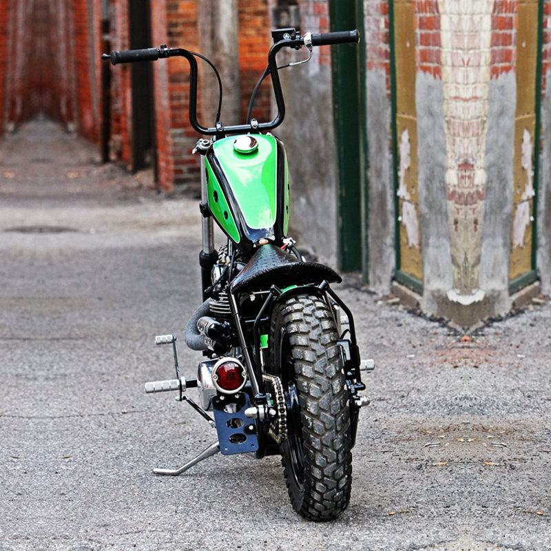 A green motorcycle parked on a street with TC Bros. Black 33 Ford Replica Side Mount Tail Light/License Plate Bracket.