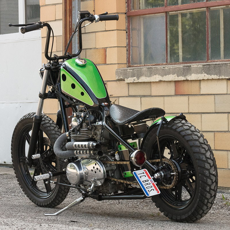 A green and black motorcycle parked in front of a building with a TC Bros. Black 33 Ford Replica Tail Light and license plate light.