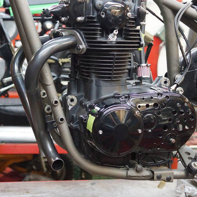A Yamaha XS650 "Double D" Exhaust System By Pandemonium is sitting on a table in a workshop.