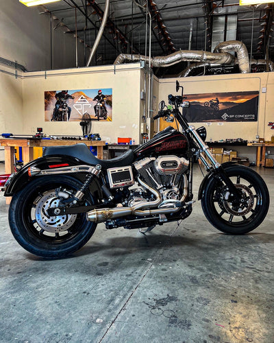 An SP Concepts Lane Splitter Exhaust 06-17 Dyna (stainless) motorcycle parked in a garage.