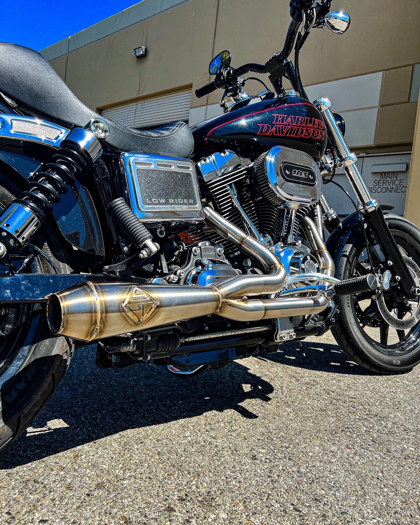 A SP Concepts Lane Splitter Exhaust 06-17 Dyna (stainless) motorcycle is parked in front of a building.