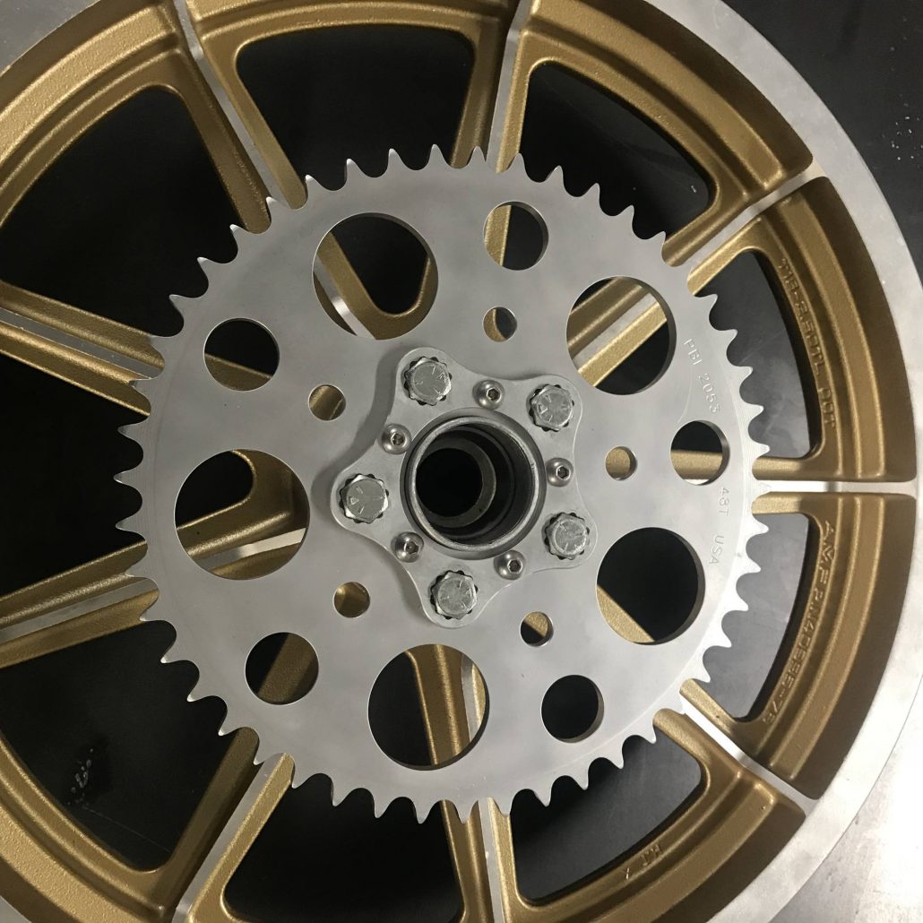 A close up of a gold motorcycle wheel with a HHB Harley Davidson Sprocket Lock System - Aluminum and bolt pattern from Hughs Handbuilt on it.