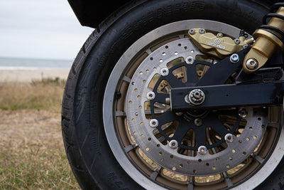A close up of a motorcycle's front wheel and rear brake, with TC Bros. 2006-2007 Harley Dyna Rear Axial Brembo Bracket Stock Rotor calipers for enhanced stopping power.