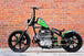 A green motorcycle parked in front of a brick wall, featuring a FirePower 530 Gold Heavy Duty O-Ring Chain 150 Links.