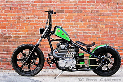 A durable green TC Bros. motorcycle parked in front of a brick wall.