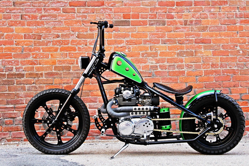 A green TC Bros. Choppers Air Spring motorcycle parked in front of a brick wall, with adjustability for vibration dampening.