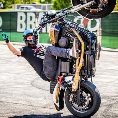 A man performing a handstand on a motorcycle, showcasing the TC Bros. 2006-2007 Harley Dyna Rear Radial Brake Bracket sportbike caliper.