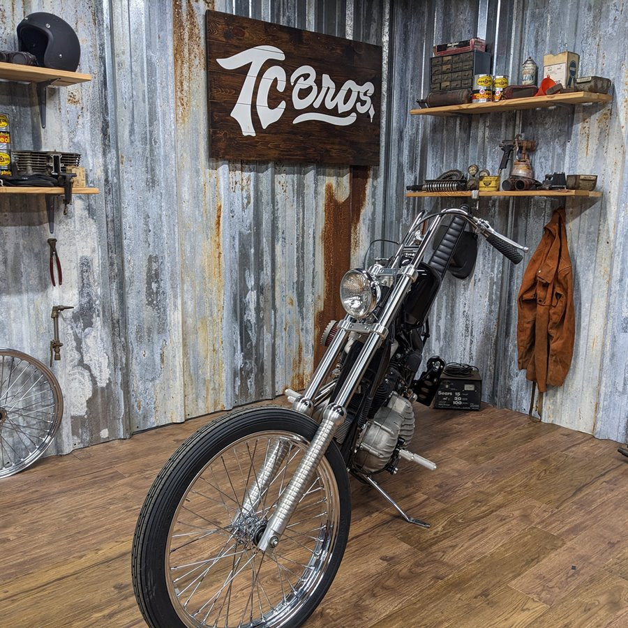 A TC Bros. Extra Narrow Triple Tree Set for 1988-2003 Harley Davidson 39mm Narrowglide front end motorcycle is parked in a room with a wooden floor.