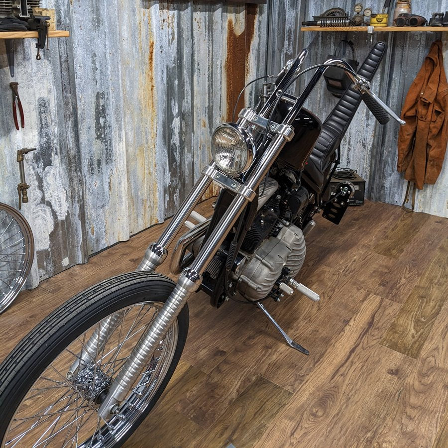 A TC Bros. Extra Narrow Triple Tree Set for 2008-2022 Harley Davidson Sportster chopper front end motorcycle is parked on a wooden floor in a garage.