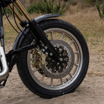 A TC Bros. Black Axial Brembo Front LH Bracket for 2000-2017 Harley Stock Rotors, featuring a black metal bracket with three holes, three screws, four washers, and a metal connector, all displayed on a white background. Ideal for high-performance brake conversions or as part of the TC Bros. product line.