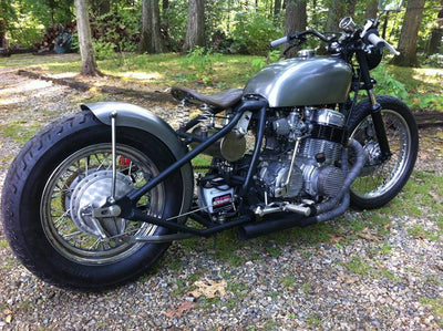 A TC Bros. Honda CB750 Weld On Hardtail Frame motorcycle parked in the woods.