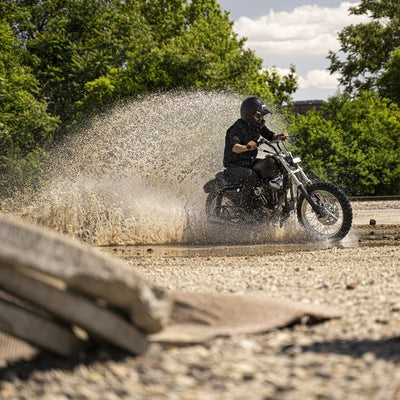 A person riding a TC Bros. Scrambler LED Headlight Kit for Harley Davidson - Single through a puddle of water.