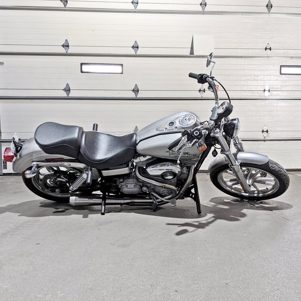 A silver TC Bros. Harley Davidson Dyna motorcycle, with an aftermarket exhaust system, parked in front of a garage.