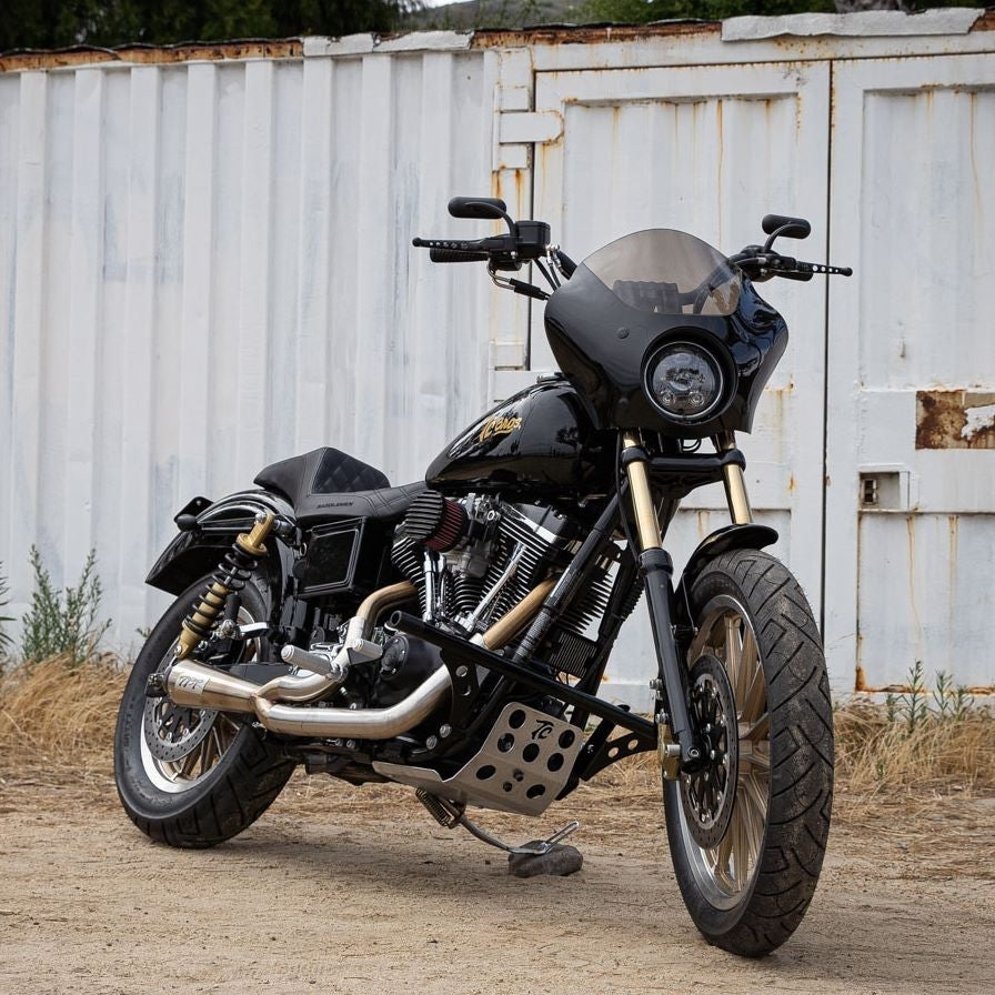 A motorcycle with TC Bros. Gold Titanium Nitride Coated Fork Tubes +2" Length 39mm for Sportster/ Dyna Narrow Glide parked in front of a building.
