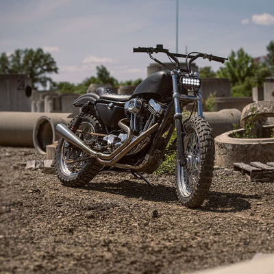 A motorcycle with a black TC Bros. Scrambler LED Headlight Kit for Harley Davidson - Single parked in a dirt field.