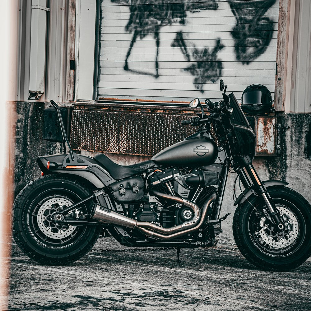 A black TC Bros. M8 Fat Bob Kickback Sissy Bar Black 2018-newer FXFB FXFBS motorcycle parked in front of a building.