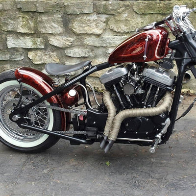 A vintage style motorcycle parked in front of a stone wall with TC Bros. heavy duty steel rear fenders, specifically the 6-1/4" Wide Spun Steel Chopper & Bobber Fender by TC Bros Choppers.