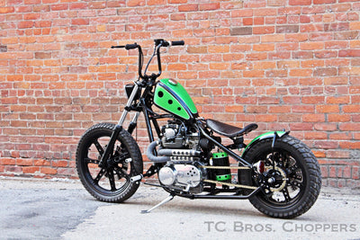 A TC Bros. Choppers Air Spring motorcycle parked in front of a brick wall with adjustability for vibration dampening as it features rubber air spring.