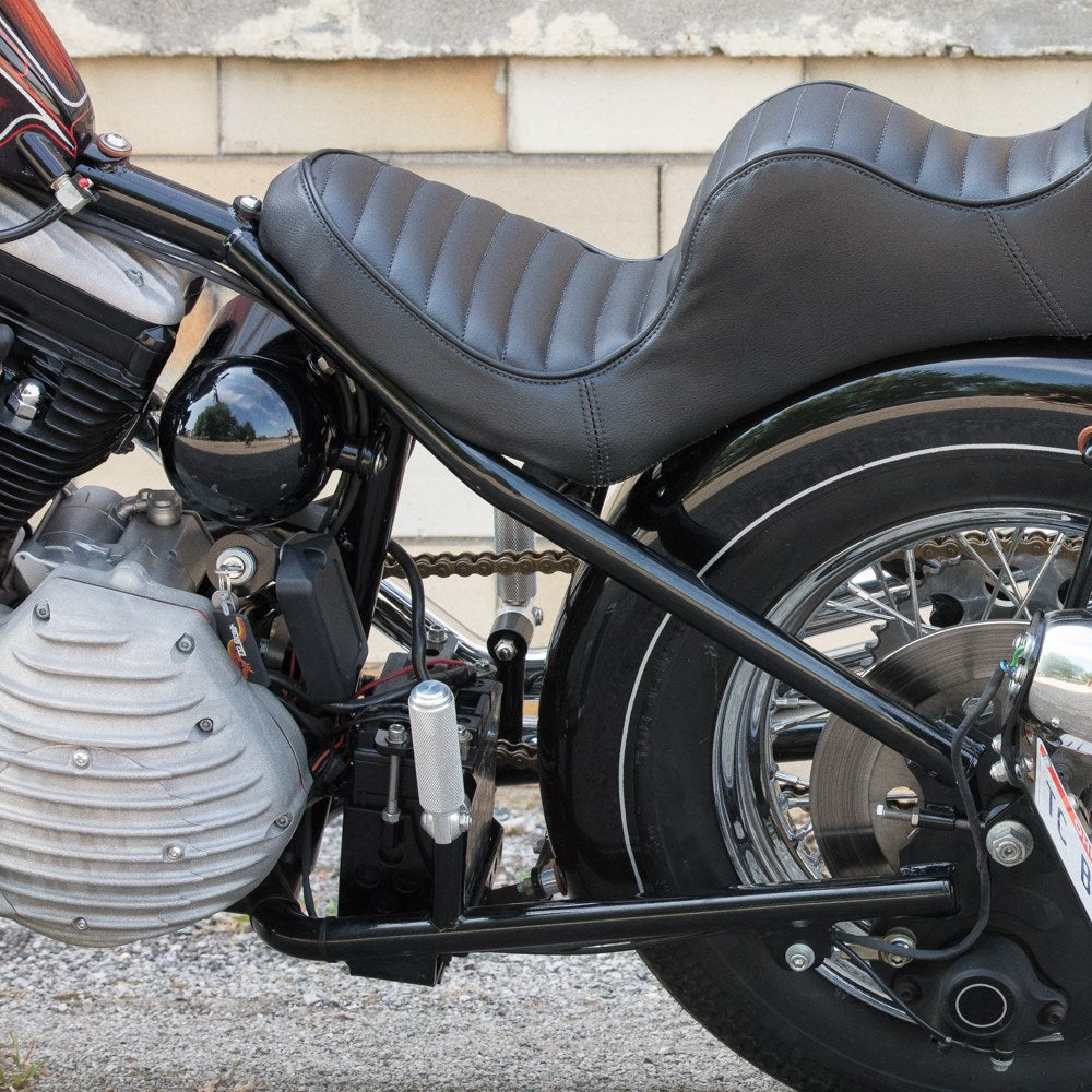 A black TC Bros. motorcycle with a TC Bros Battery Box Mounting Kit for Stock Tire '82-'03 Sportster Hardtail mounted tire parked in front of a building.