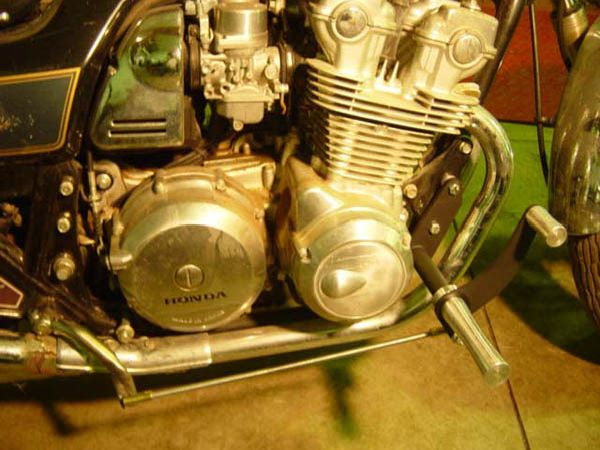The engine of a TC Bros. Honda DOHC CB750 Forward Controls Kit motorcycle is on display in a garage.