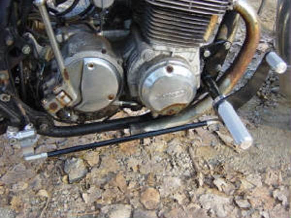 A TC Bros. Honda SOHC CB750 Forward Controls Kit with a rusty engine sitting on a dirt road.