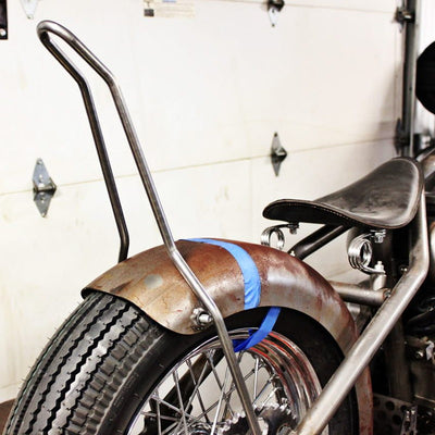 A TC Bros. Kickback DIY Sissy Bar Kit with blue tape on it is sitting in a garage.