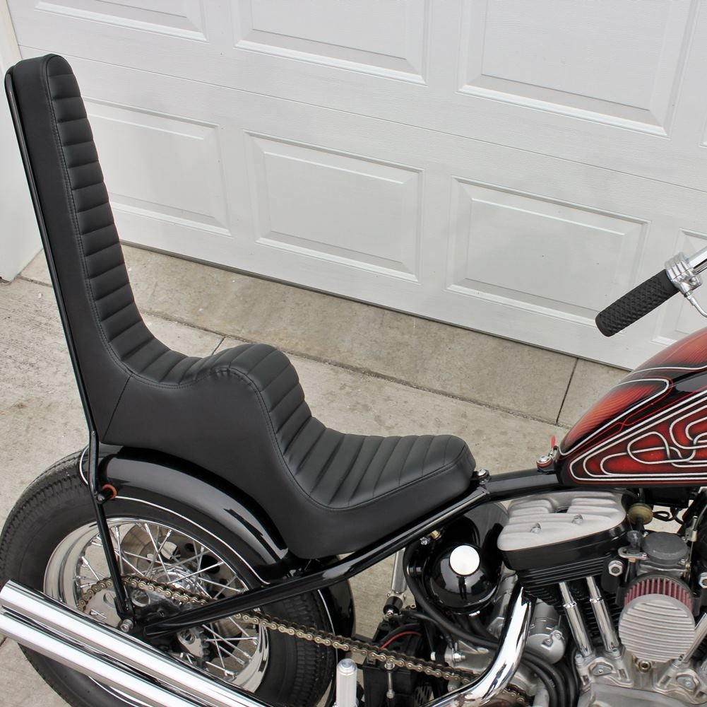 A TC Bros. King & Queen Hardtail Seat Black Pleated motorcycle is parked in front of a garage.