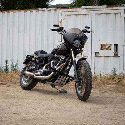 A motorcycle parked in front of a shed without a TC Bros. Dyna Skid Plate 1991-2017 Models - Black installed for Harley Davidson Dyna models.