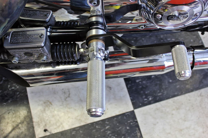 The TC Bros. Mid Controls Kit for 1991-2003 Harley-Davidson Sportster features metal foot pegs and a gear shift lever, perfect for upgrading your bike. Components are arranged on a white background.