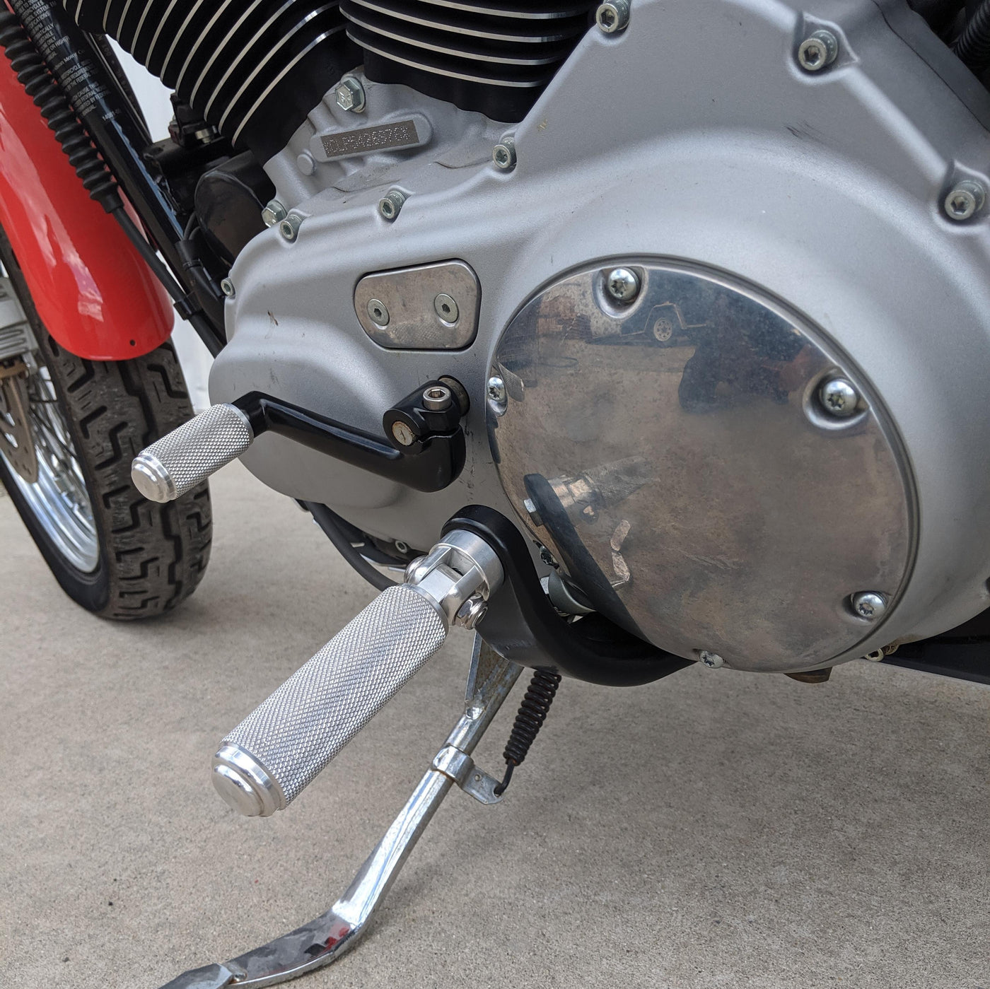 A close up of a TC Bros. Sportster Mid Controls Kit (NO PEGS) fits 2004-2013 on a Harley Davidson motorcycle with a red handlebar.